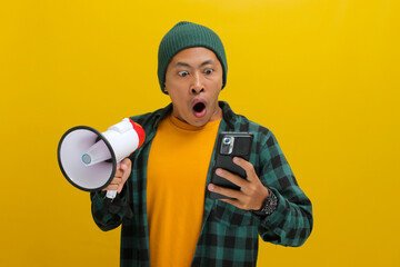 Surprised Asian man in a beanie and casual clothes stares at his phone with wide eyes, seemingly...