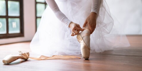 Ballerina in ballet shoes. Asian girl tying ribbons of toe shoes. ballet dancer preparing and wearing ballet shoes in dance studio prepares for a rehearsal.