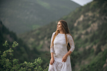 A woman in a white dress stands on a mountain top