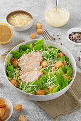Caesar salad with lettuce, grilled chicken breast, parmesan cheese and croutons in a bowl on a gray concrete background. Copy space
