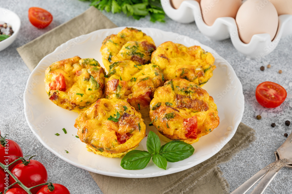 Wall mural egg muffins or egg bites with bacon, cheese, vegetables and herbs on a white plate on a concrete bac