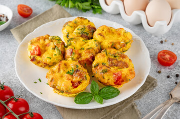 Egg muffins or egg bites with bacon, cheese, vegetables and herbs on a white plate on a concrete background. Healthy breakfast.