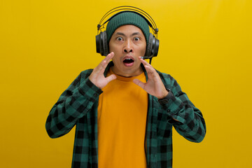 Asian man in a beanie and casual clothes, wearing headphones, looks shocked with his mouth agape...