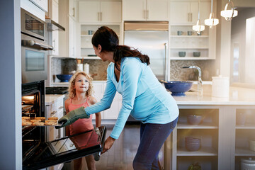 Mother, daughter and cookies in oven for cooking in kitchen with learning, bonding and fun in home...