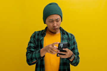 An unhappy Asian man, dressed in a beanie hat and casual shirt, holds a phone, visibly upset, displaying sadness, worry, or perhaps shedding tears in reaction to distressing news received online