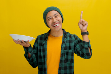 Young Asian man, wearing a beanie hat and casual shirt, raises his finger in a eureka moment while...