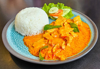 A vibrant plate of red curry with chicken, served alongside a mound of white rice and fresh salad