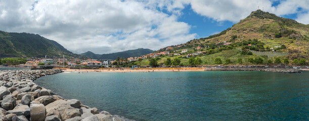 Panoramic view of Machico bay with golden sand beach, palm trees and houses surrounded by green mountains. Machico is popular resort town at east coast of Madeira