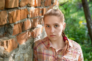 Portrait of a sad pretty teenage girl who suffers from loneliness and frequent conflicts with her older brother and parents. A teenage girl in front of old house with broken bricks