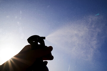 A woman's hand sprays an air freshener against the sky.