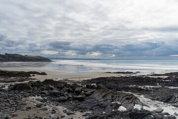 Sous un ciel nuageux, une formation rocheuse se dévoile à marée basse, entre sable et falaise, sur la pittoresque presqu'île de Crozon, créant une atmosphère mystique et captivante.