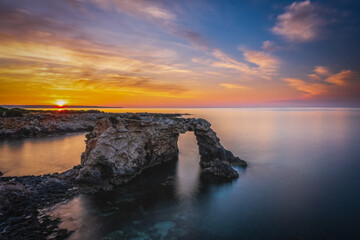 Rocky coastline with a natural arch at punta Asparano, near Siracusa. Sunrise time, long exposure...