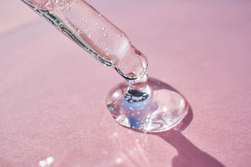 Pipette with serum shimmering in the sun on a pink background.