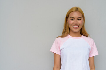 Obraz premium Portrait of beautiful Asian girl with blonde hair smiling against plain background
