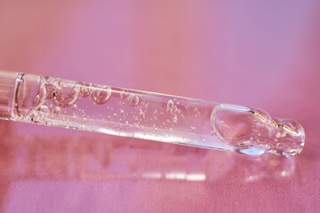 Pipette with serum shimmering in the sun on a pink background.