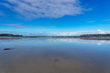 "Reflets du ciel bleu et des nuages sur le sable mouillé d'une plage de la presqu'île de Crozon, une scène harmonieuse et changeante.