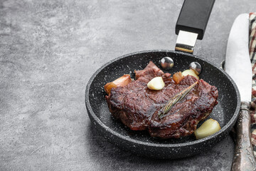 Fried beef steak with herbs in small frying pan on gray background