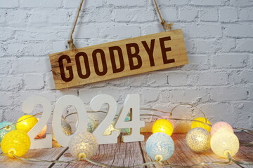 Goodbye 2024 letters with LED cotton balls decoration on wooden background