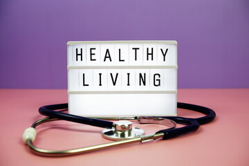 Healthy Living letterboard text on LED Lightbox and stethoscope on pink and purple background