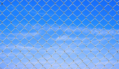 Metal chainlink wire mesh fence against white clouds on blue sky background