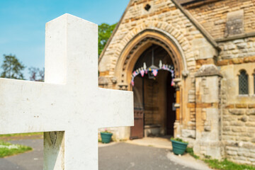 Shallow focus of a marble crucifix seen outside a typical English church. Union Jack bunting can be seen within the entrance, the church celebrating its centenary.