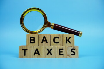 Back Taxes with wooden blocks alphabet letters and Magnifying glass on blue background