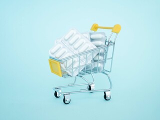 A grocery cart with pills and colored capsules in blisters on a blue background. The concept of buying medicines at a pharmacy