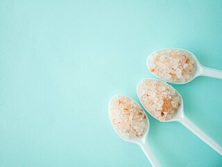 Pink Himalayan salt in large crystals in plastic spoons on a blue background. A place for the text