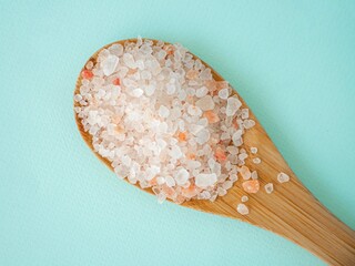Pink Himalayan salt in large crystals in a wooden spoon on a blue background