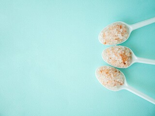 Pink Himalayan salt in large crystals in plastic spoons on a blue background. A place for the text