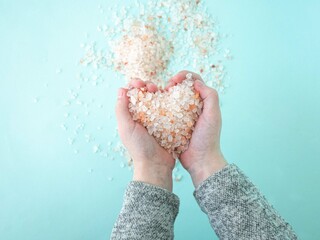 In the hands of a child, pink Himalayan salt in the shape of a heart. Salt in large crystals