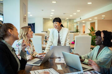 Multiethnic female colleagues discussing work with laptops in a modern office