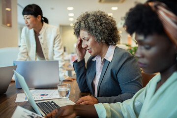 Stressed businesswoman with headache working with colleagues in office