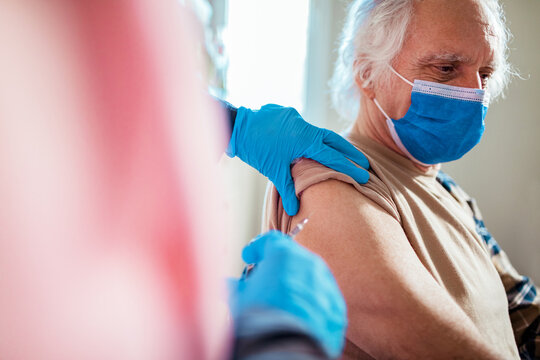 Senior man in face mask getting vaccinated at home