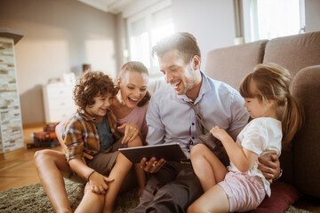 Parents and children using tablet on living room sofa