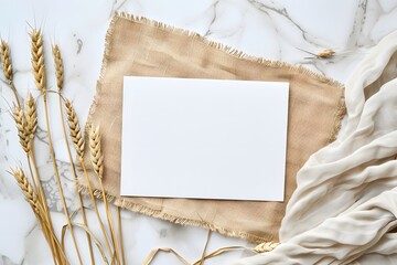 Elegant white invitation card with golden wheat on a marble background, draped with silk fabric. Flat lay composition with copy space. Wedding and elegant event concept for design and print.