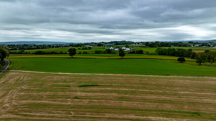 Naklejka premium This aerial view showcases a striking rural landscape under an overcast sky, featuring contrasting patches of lush green fields and harvested areas.
