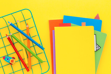Stack of school notebooks and blank yellow notebook cover on yellow background. Top view.