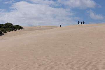 Arid sand dunes in summer with tourist walking up in Punta Paloma on a bright sunny day with blue sky