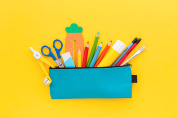 Pencil case with school supplies on yellow background. Top view.
