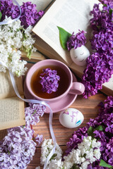 Easter and eggs with painting Christ is Risen, a cup of tea and lilac flowers, spring still life.