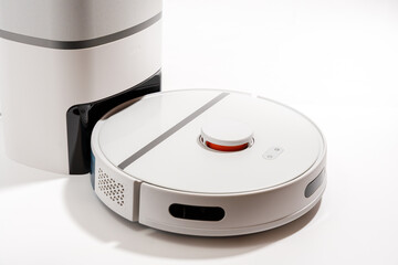 A white robot vacuum cleaner sits on a white surface. The robot is white and black with a red...