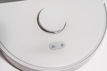 A white robot vacuum cleaner with a button on the side. The button is labeled 
