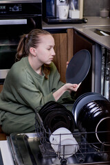 Woman unloading clean dishes from dishwasher at home