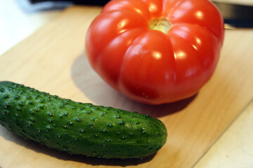 Close-up of cucumbers and tomatoes - fresh vegetables from the farmer's garden and greenhouse, healthy food, in the kitchen on the table on a wooden board next to a ceramic black knife
