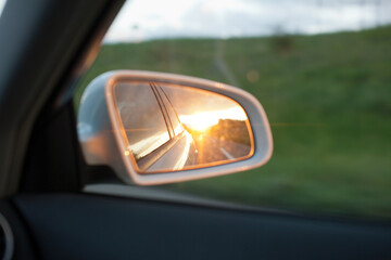 View on the rear mirror of a driving car in the sunset in the nature