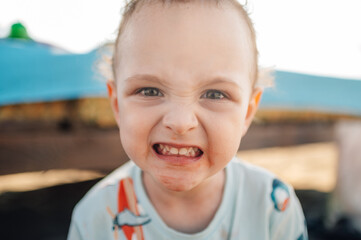 A boy with angry and messy face from food is looking at the camera.
