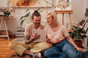 Happy artistic hipster couple sitting on floor at atelier and painting