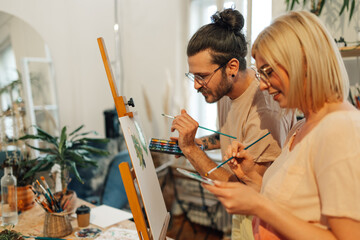 Side view of artist couple painting on canvas at creative art studio.