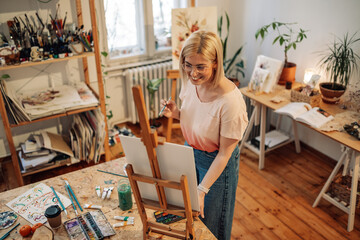 Artistic female hipster artist painting on easel at creative art studio
